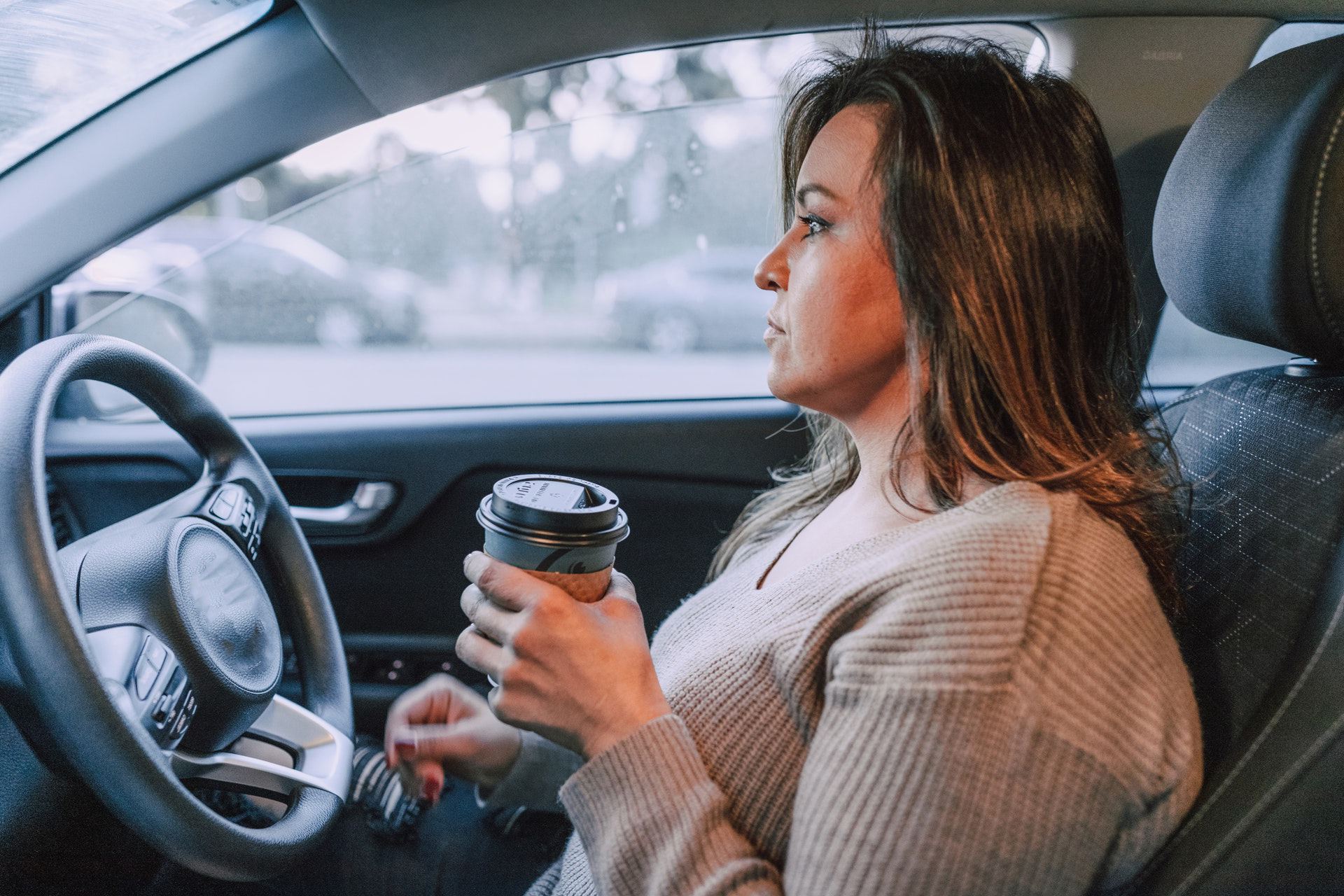 A woman in a car with a travel coffee cup